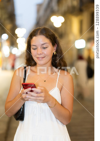 Young woman with phone in her hands walking down the street 128899339