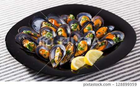 Steamed mussels on black dish with lemon 128899359