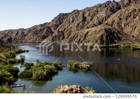 Kayakers on a Calm River by Rocky Mountains on the Colorado River in Arizona USA Kayakers on a Calm River by Rocky Mountains on the Colorado River in Arizona USA 128899570