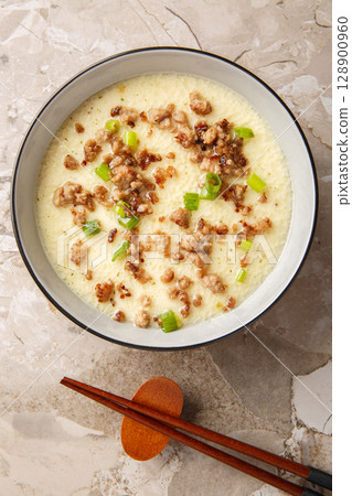 homemade steamed egg with crispy minced pork and green onion closeup in the bowl. Vertical top view 128900960