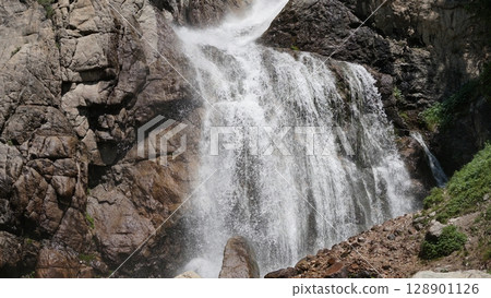 Powerful mountain waterfall cascading down rocky cliff face Powerful mountain waterfall cascading down rocky cliff face 128901126