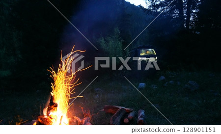 Campfire burning brightly in wilderness with off road vehicle in background Campfire burning brightly in wilderness with off road vehicle in background 128901151