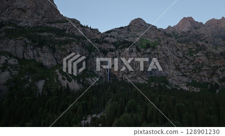 Waterfall cascading down rocky mountainside at twilight in the wilderness 128901230