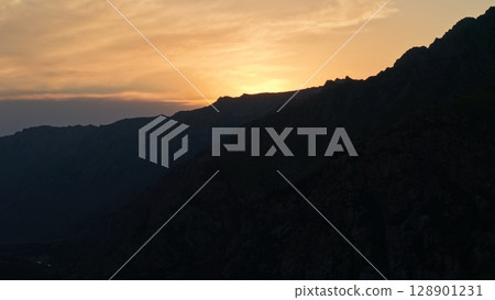 Sunset illuminating mountain valley with river flowing below 128901231