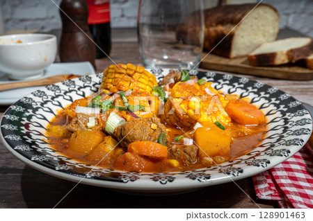 Hearty beef stew called carbonada with corn on the cob enjoyed with wine and bread 128901463