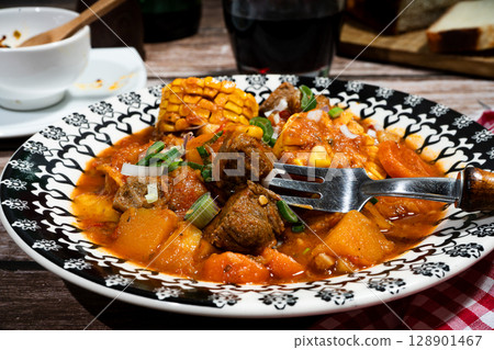 Fork picking up beef stew called carbonada with butternut squash, corn on the cob, and carrots 128901467