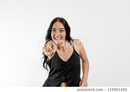 Young latin woman pointing and laughing on white background 128901488