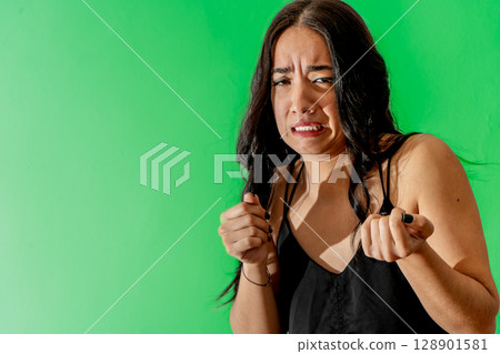 Young latin woman showing disgust expression on green background 128901581