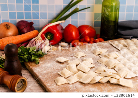 Fresh ravioli with flour on wooden cutting board with vegetables and spices Fresh ravioli with flour on wooden cutting board with vegetables and spices 128901614
