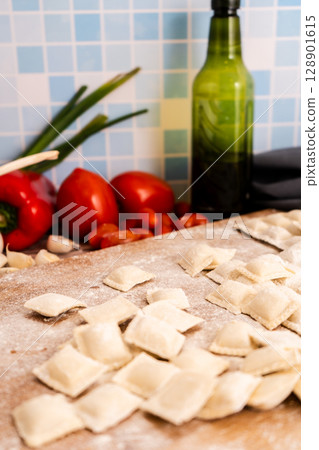 Fresh ravioli with flour on wooden cutting board with vegetables and spices. Vertical Orientation 128901615