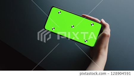 young woman sitting at the black table near window and holding smartphone with horizontal green screen young woman sitting at the black table near window and holding smartphone with horizontal green screen 128904591