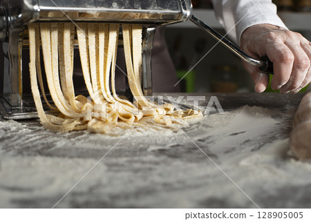 Caucasian female hands making fettuccine noodles using mechanical pasta machine 128905005