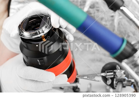 the hands of the master with gloves and a broken lens of a professional camera. the hands of the master with gloves and a broken lens of a professional camera. 128905390