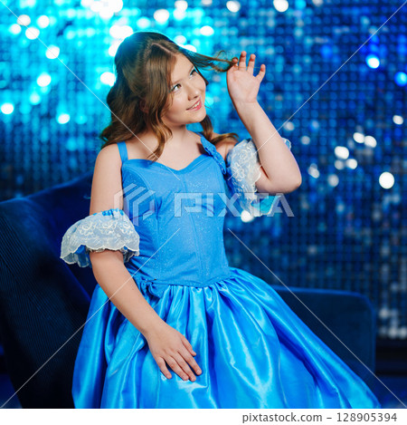 Cute teenage girl in blue doll dress posing against sequin wall background Cute teenage girl in blue doll dress posing against sequin wall background 128905394