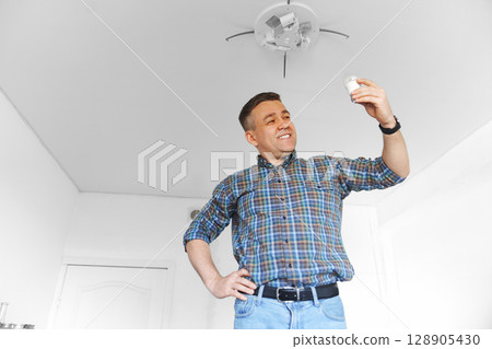 A cheery man in a plaid shirt replacement of light bulbs in a ceiling lamp 128905430