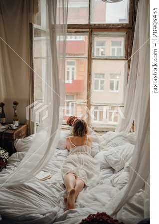 a young blonde woman in a white dress on white sheets 128905435