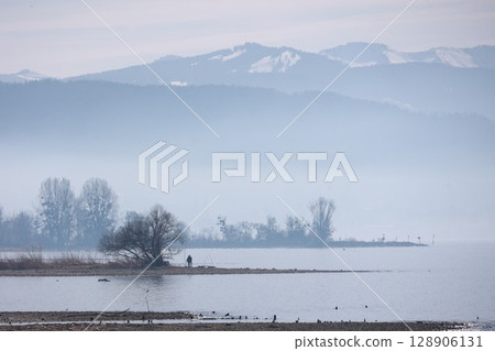 A man is walking on a beach near a body of water 128906131
