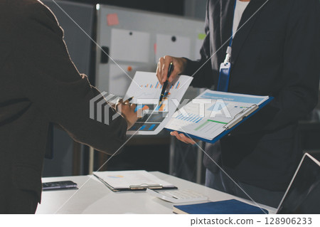 Focused young businessman signing agreement with skilled lawyer in eyeglasses. Concentrated financial advisor showing place for signature on paper contract document to male client at meeting in office Focused young businessman signing agreement with skilled lawyer in eyeglasses. Concentrated financial advisor showing place for signature on paper contract document to male client at meeting in office 128906233