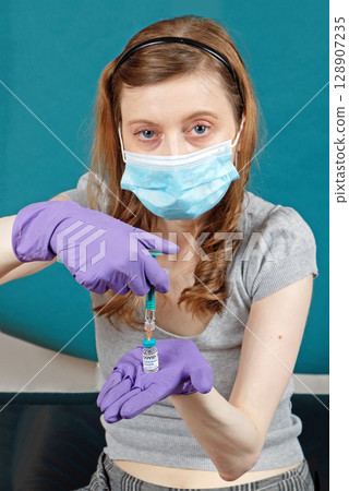 Young nurse preparing syringe for administering covid-19 vaccine 128907235