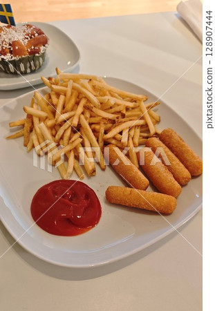 Plate with crispy french fries, breaded cheese sticks and a serving of ketchup on a white table 128907444