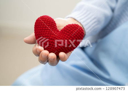 Asian elder senior woman patient holding red heart in hospital. Asian elder senior woman patient holding red heart in hospital. 128907473