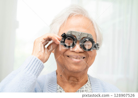 Optometrist checking Asian elderly woman ophthalmic vision eye test and using optical trial frame. 128907526