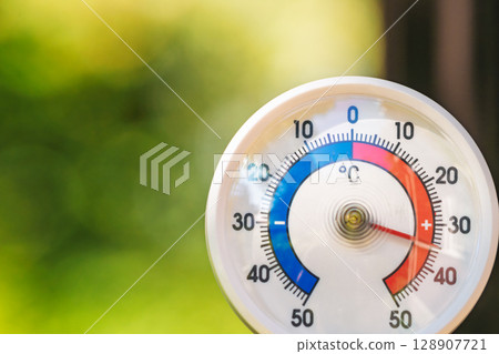 Outdoor thermometer showing high summer temperature in Celsius with blurred green garden background Outdoor thermometer showing high summer temperature in Celsius with blurred green garden background 128907721