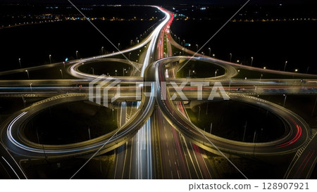 Aerial view of multi-level highway interchange glowing at night with organized traffic flow and symmetrical design. Generative AI. Aerial view of multi-level highway interchange glowing at night with organized traffic flow and symmetrical design. Generative AI. 128907921