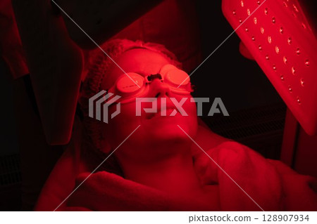 Woman relaxing with light therapy treatment in a wellness center 128907934