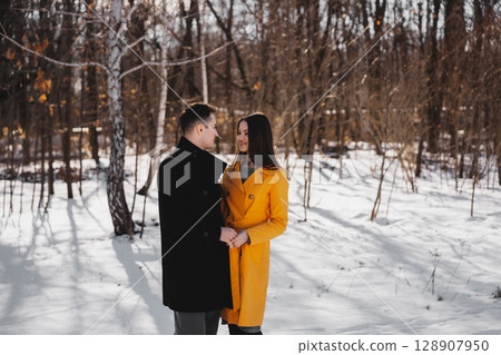 Couple enjoys a winter moment in a snowy forest under bright sunlight 128907950