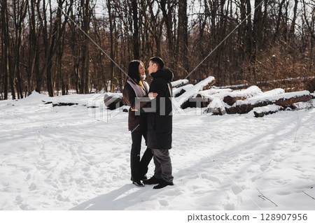 Couple embraces in a snowy forest during winter afternoon 128907956