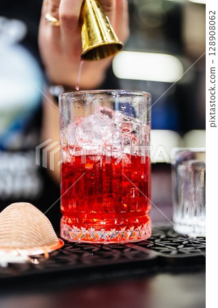 Crafting a vibrant cocktail with precision at a lively bar in the evening 128908062