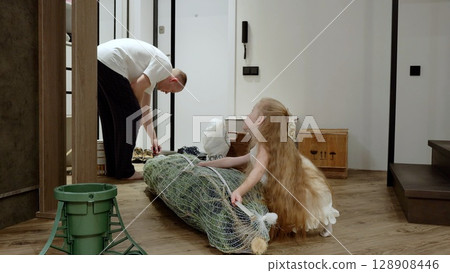 Cheerful father helping young daughter assembling artificial christmas tree, decorating living space with festive spirit, sharing warm family moment during holiday season 128908446