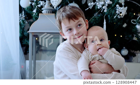 Two young brothers are standing in front of a festive christmas tree, savoring the holiday season with their family. A day with family before Christmas. New Year's Eve with family Two young brothers are standing in front of a festive christmas tree, savoring the holiday season with their family. A day with family before Christmas. New Year's Eve with family 128908447