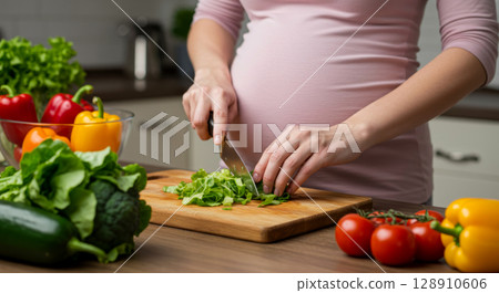 Pregnant woman chopping fresh vegetables in kitchen. Healthy eating, prenatal nutrition, and maternal wellness. 128910606