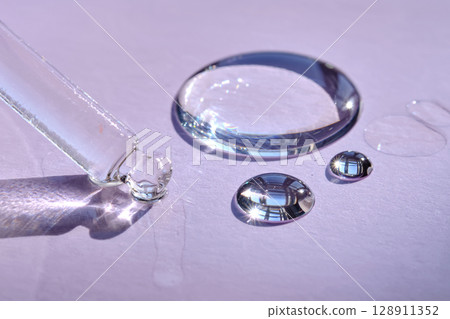 A drop of serum with a pipette on a purple background. 128911352