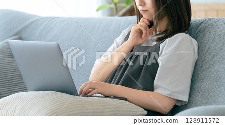 坐長沙發和使用計算機的婦女 坐長沙發和使用計算機的婦女 128911572