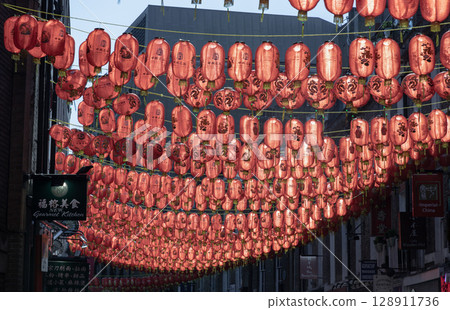 View of Red chinese lanterns hanging in rows above the street, strung between buildings. View of Red chinese lanterns hanging in rows above the street, strung between buildings. 128911736
