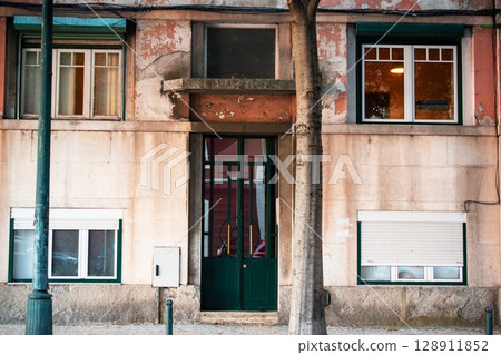 Facade of a weathered building with a green door and multiple windows. Facade of a weathered building with a green door and multiple windows. 128911852