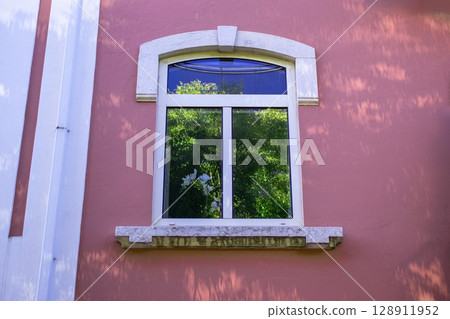 Window with white frame on a pink building exterior with decorative trim. Window with white frame on a pink building exterior with decorative trim. 128911952