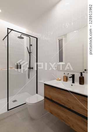 Modern bathroom with a glass shower, wooden vanity, and minimalist decor. Neutral colors create a clean and spacious atmosphere. 128911962