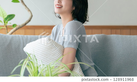 Smiling woman sitting on sofa in living room Smiling woman sitting on sofa in living room 128911968