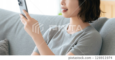 Smiling woman sitting on sofa and using smartphone Smiling woman sitting on sofa and using smartphone 128911974
