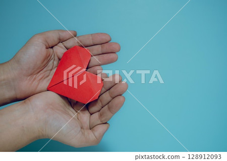 Cupped Hands Holding Red Origami Heart on Blue 128912093