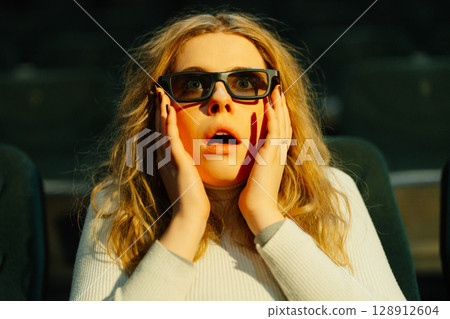 Surprised woman in 3D glasses reacts during a movie screening at theater 128912604