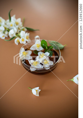 Tea composition with green tea and jasmine flowers on a brown background Tea composition with green tea and jasmine flowers on a brown background 128912660