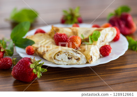 Homemade pancakes with cottage cheese filling and berries on a wooden table Homemade pancakes with cottage cheese filling and berries on a wooden table 128912661