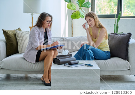 Sad teenage girl student talking with social psychologist, therapist, counselor 128913360