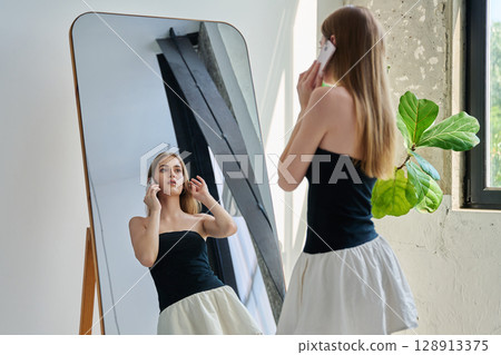 Young beautiful fashionable woman talking on phone, standing near mirror Young beautiful fashionable woman talking on phone, standing near mirror 128913375