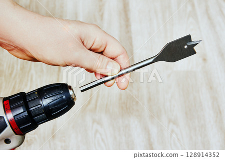 Spade drill bit being inserted into chuck of cordless screwdriver closeup shows preparation for drilling tasks with flat cutting attachment. Spade drill bit being inserted into chuck of cordless screwdriver closeup shows preparation for drilling tasks with flat cutting attachment. 128914352